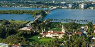 Aerial view of a waterfront estate with pool, lawns, and palm trees